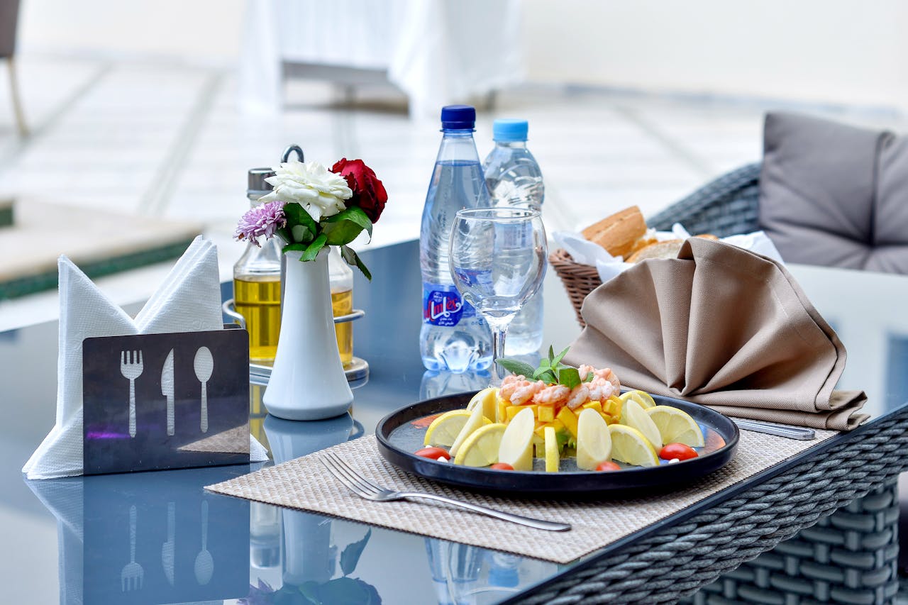 A stylish outdoor restaurant table featuring a seafood dish with lemon slices, bottled water, and decorative cutlery.